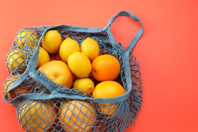 Photo of String bag with oranges and lemons on red background, top view