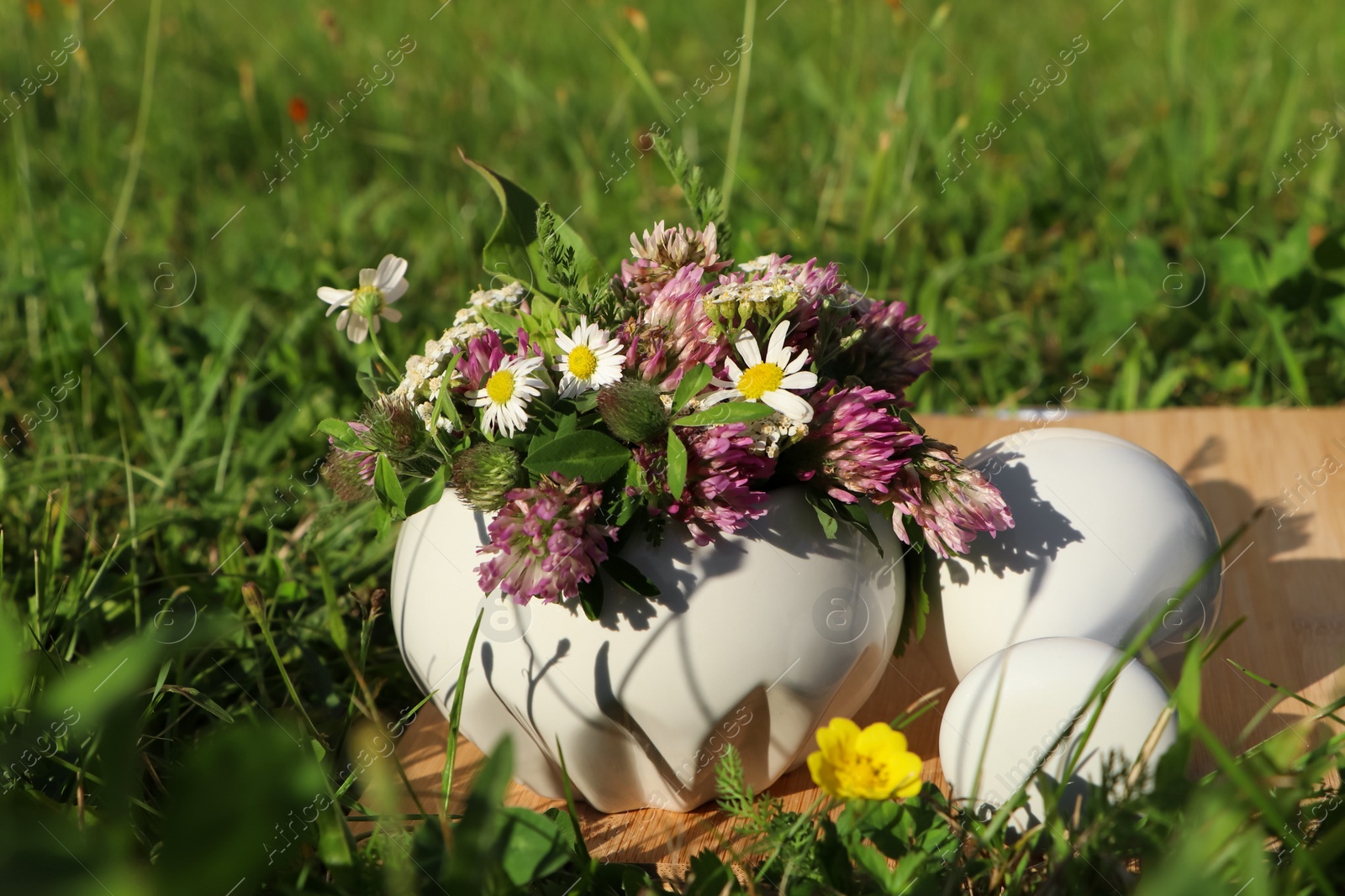 Photo of Ceramic mortar with pestle, different wildflowers and herbs on wooden board in meadow