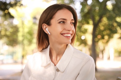Young woman with wireless headphones listening to music in park