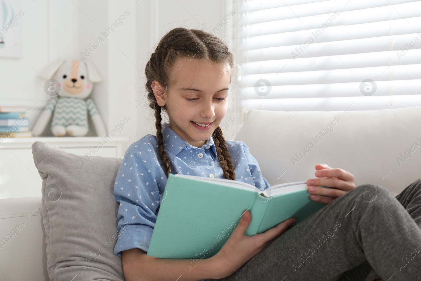 Photo of Cute little girl reading book on sofa at home