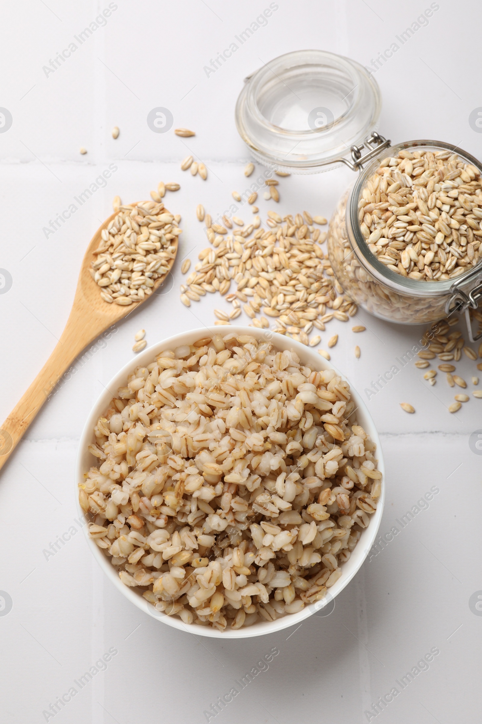 Photo of Delicious pearl barley served on white tiled table, flat lay