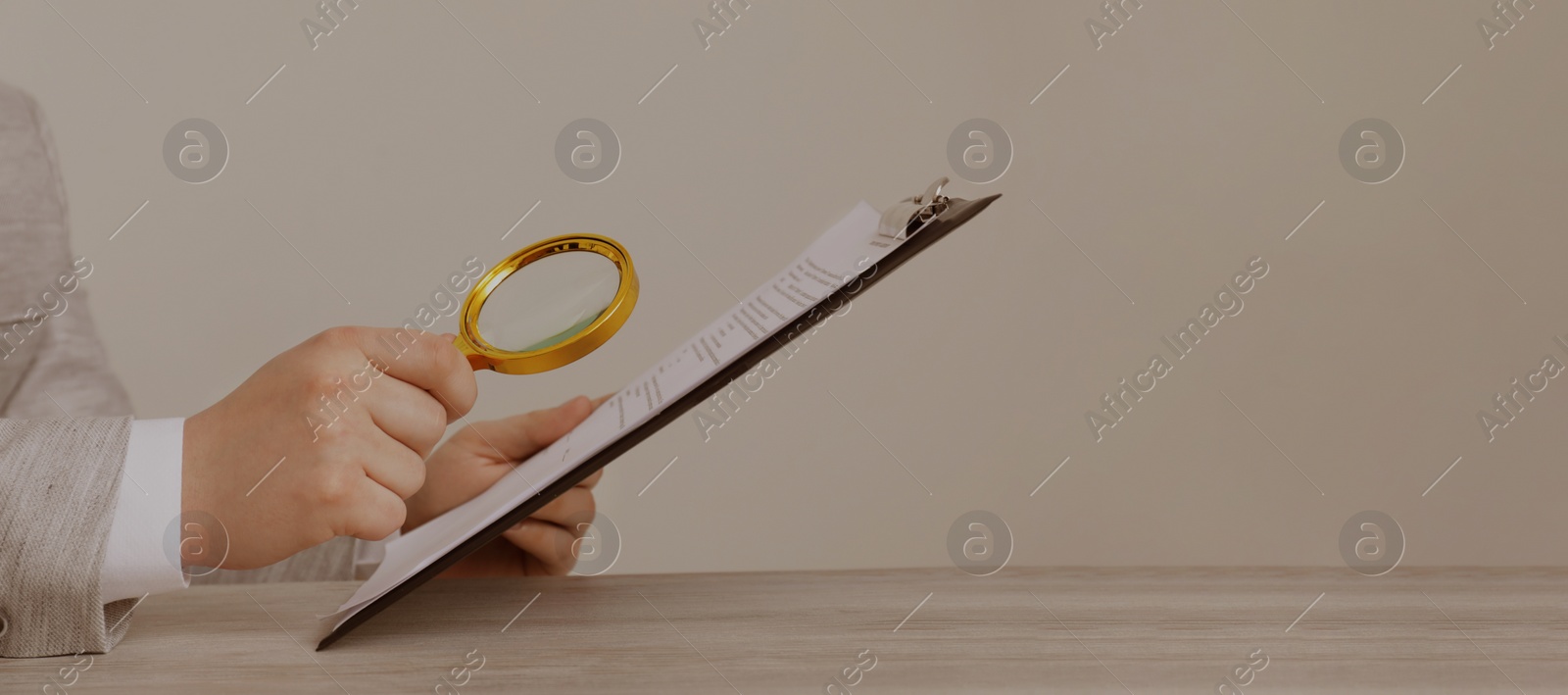 Image of Man looking at documents through magnifier at wooden table, closeup. Banner design with space for text