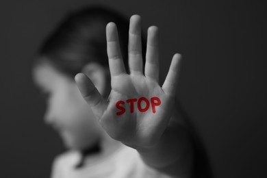 Image of No child abuse. Girl showing hand with written Stop on palm, selective focus. Black and white effect