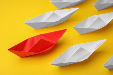 Group of paper boats following red one on yellow background, above view. Leadership concept