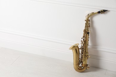 Photo of Beautiful saxophone on floor near white wall indoors, space for text