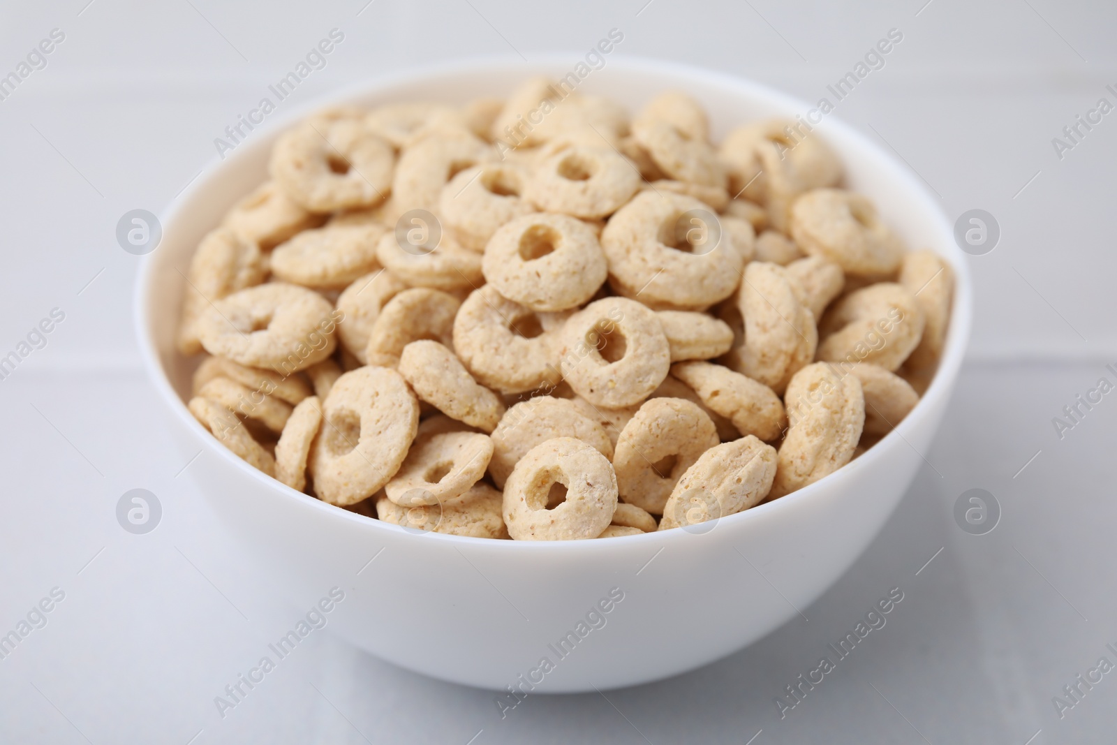 Photo of Tasty cereal rings in bowl on white table, closeup