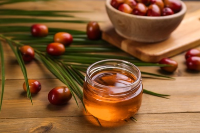 Palm oil in glass jar, tropical leaf and fruits on wooden table