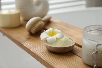 Photo of Wooden tray with spa products and plumeria flower on bath tub, closeup