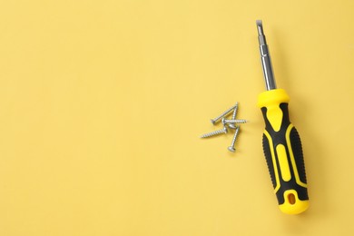 Photo of Screwdriver with black handle and screws on light yellow background, flat lay. Space for text