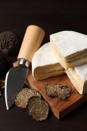 Delicious cheese, fresh black truffles and knife on wooden table
