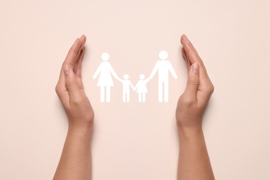 Image of Woman holding hands around paper silhouette of family on light pink background, top view. Insurance concept