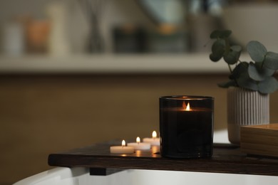 Photo of Beautiful burning candles and eucalyptus branches on wooden tray in room, space for text