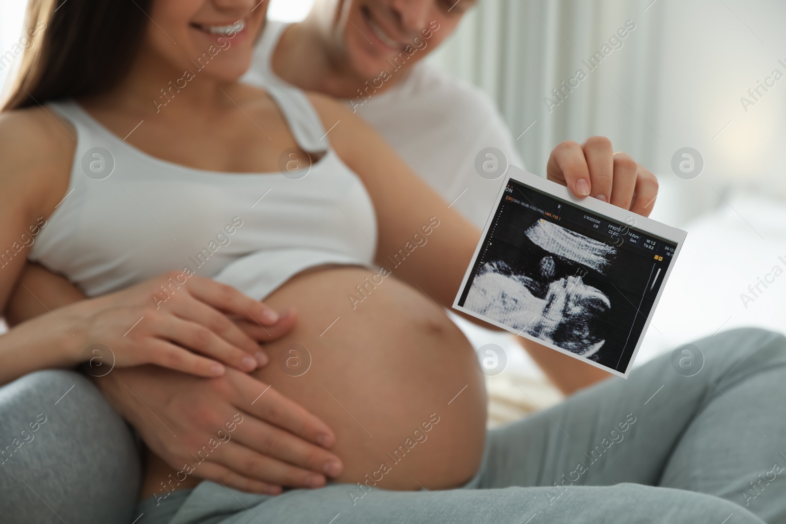 Photo of Young pregnant woman and her husband with ultrasound picture of baby indoors, closeup