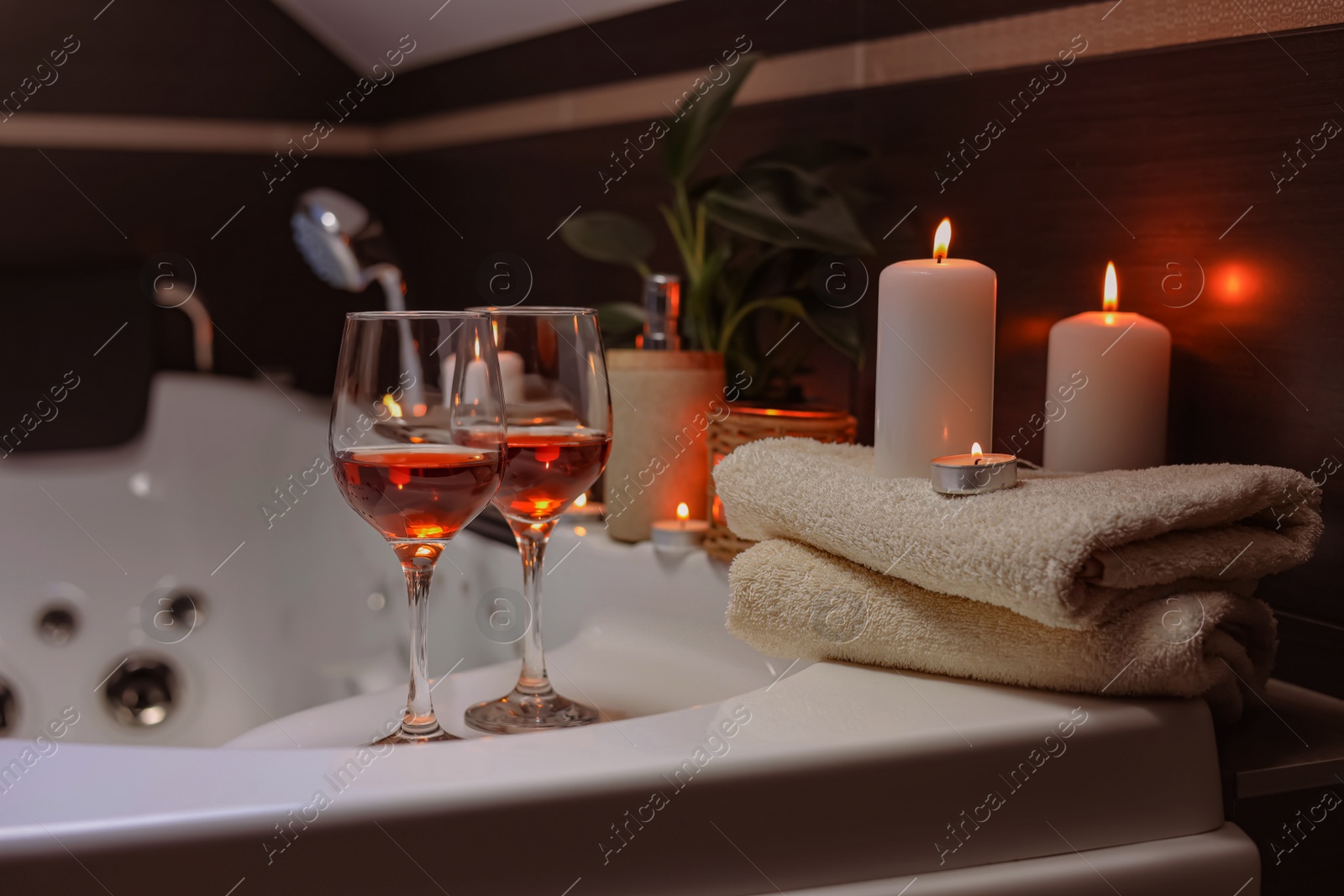 Photo of Bathtub with glasses of wine and candles indoors. Romantic atmosphere