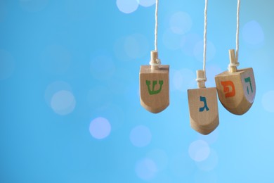 Photo of Hanukkah celebration. Wooden dreidels with jewish letters hanging on twine against light blue background with blurred lights, space for text