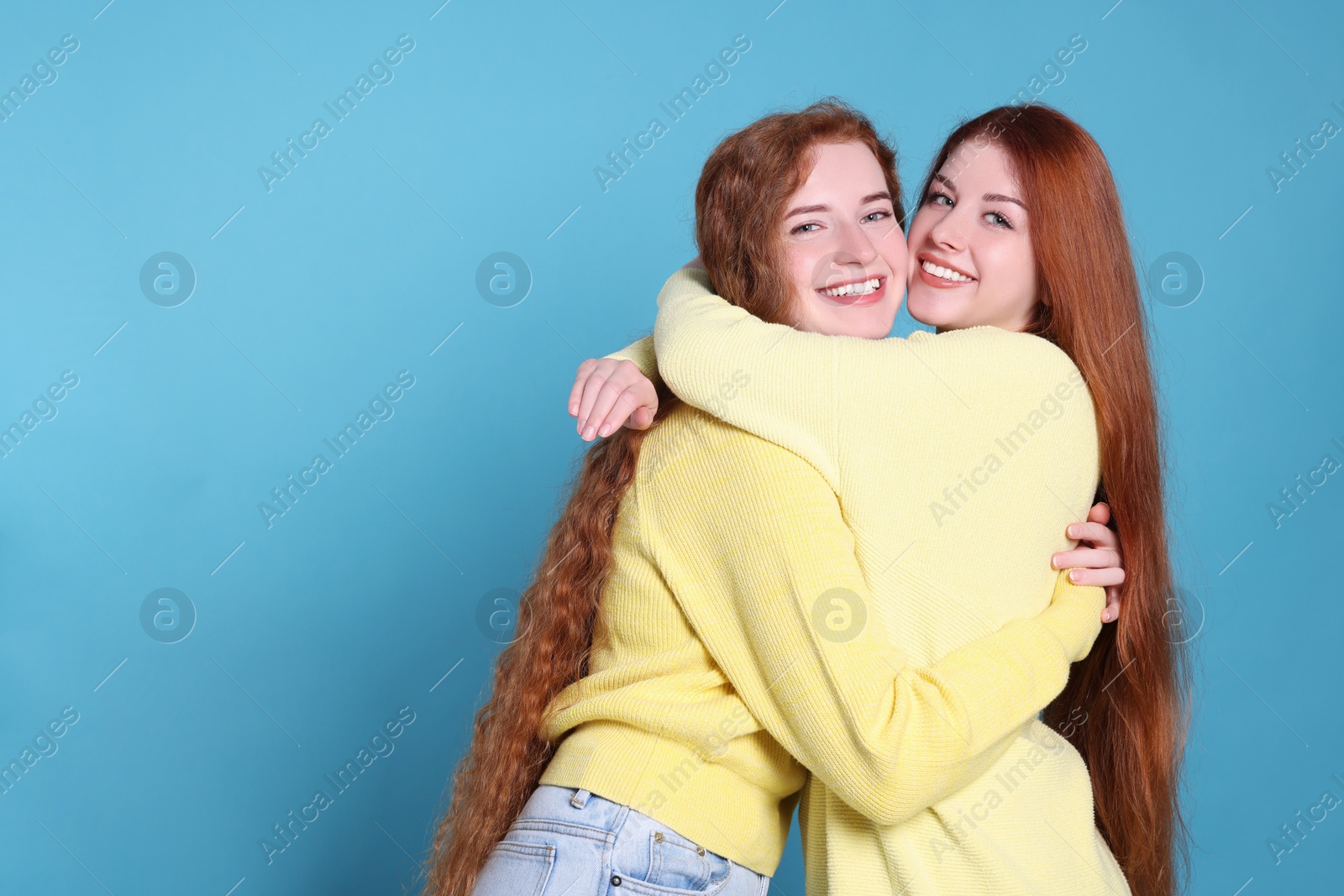 Photo of Portrait of beautiful young redhead sisters on light blue background. Space for text