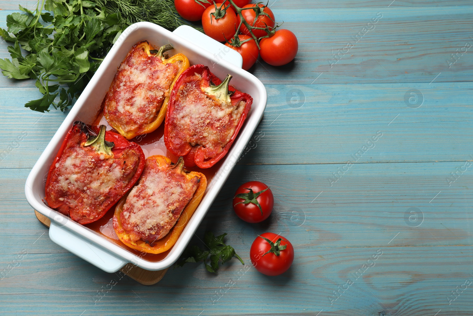 Photo of Tasty stuffed peppers in dish and ingredients on light blue wooden table, flat lay. Space for text