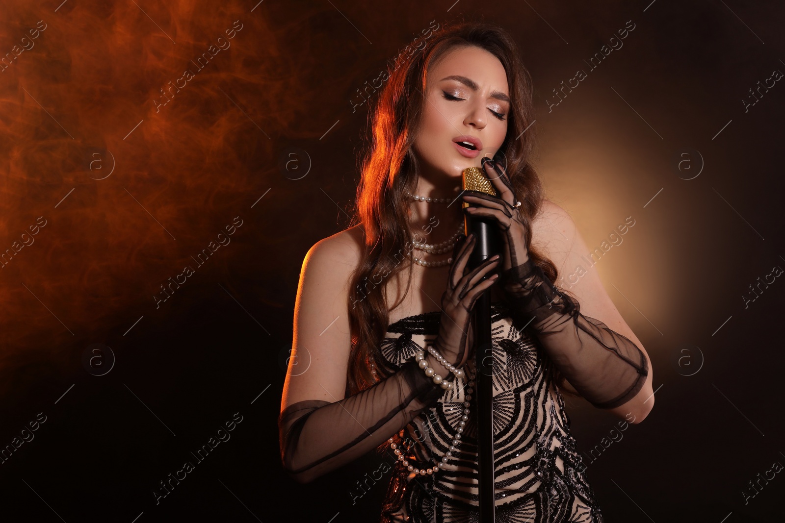 Photo of Beautiful young woman with microphone singing in color lights and smoke