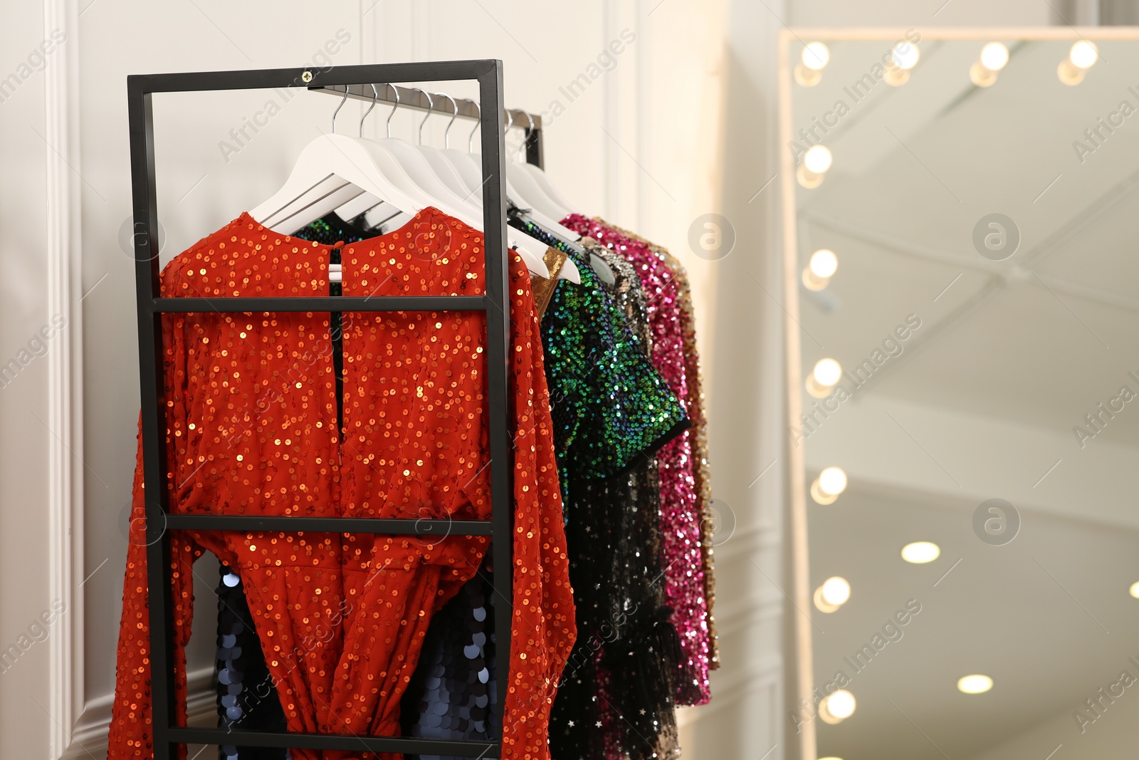 Photo of Clothing rack with colorful sequin party dresses on hangers near mirror in boutique, space for text