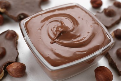 Photo of Bowl with tasty paste, chocolate pieces and nuts on white table, closeup