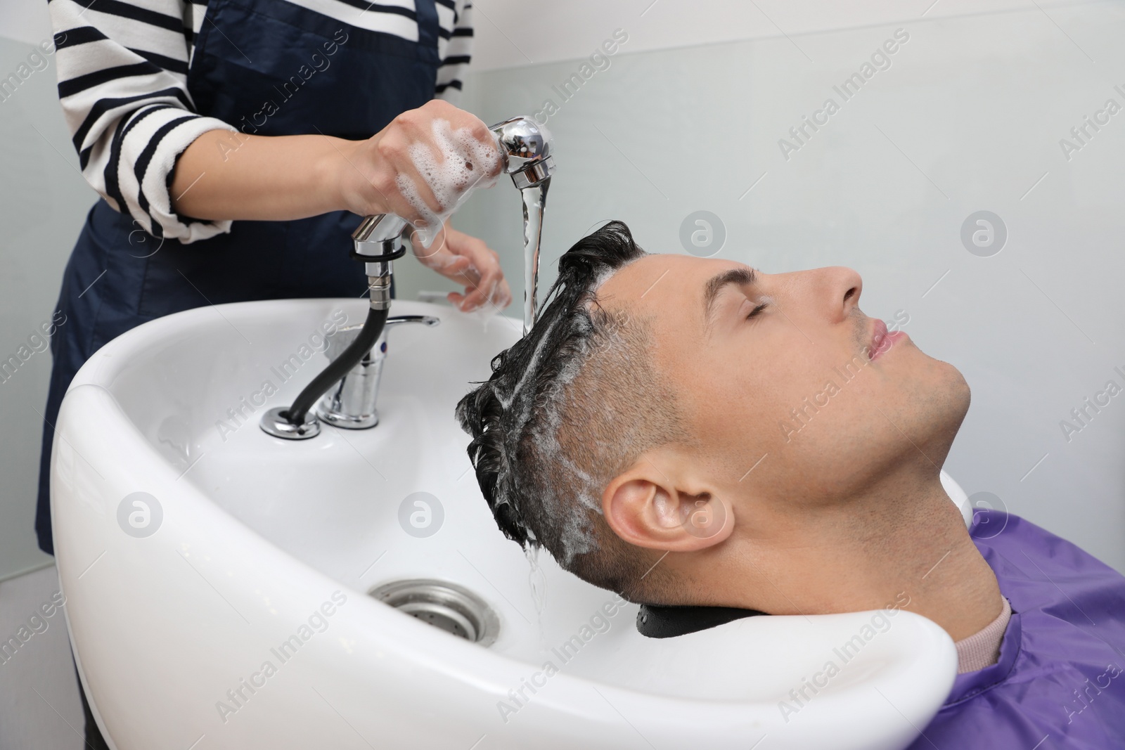 Photo of Professional hairdresser washing client's hair at sink in salon, closeup