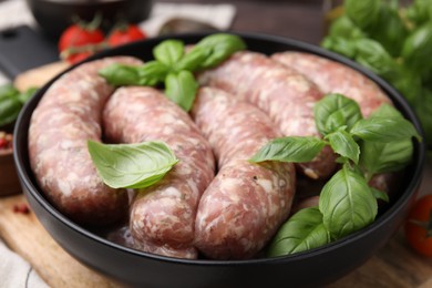 Photo of Raw homemade sausages and basil leaves on table, closeup