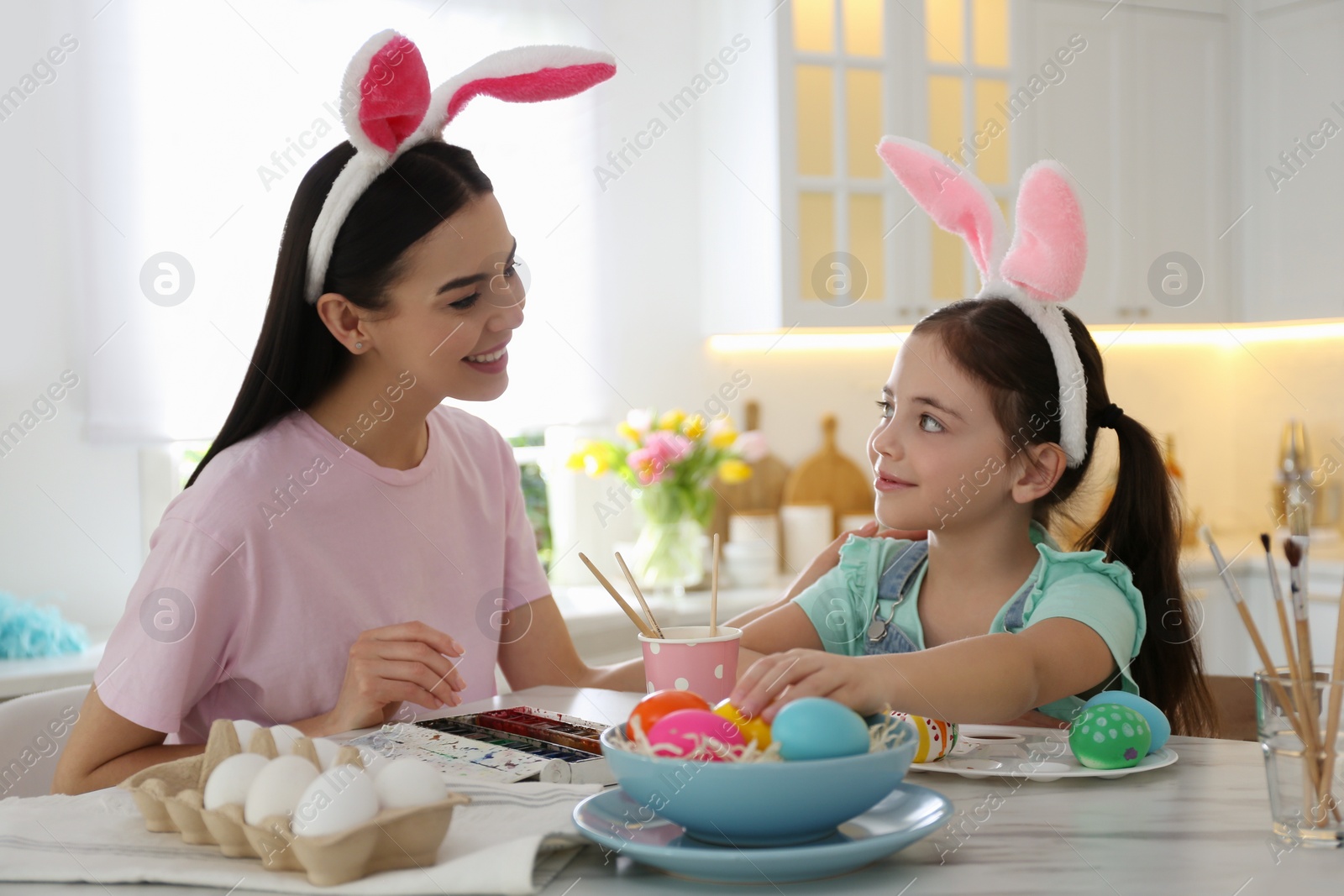 Photo of Happy mother with her cute daughter painting Easter eggs at table in kitchen