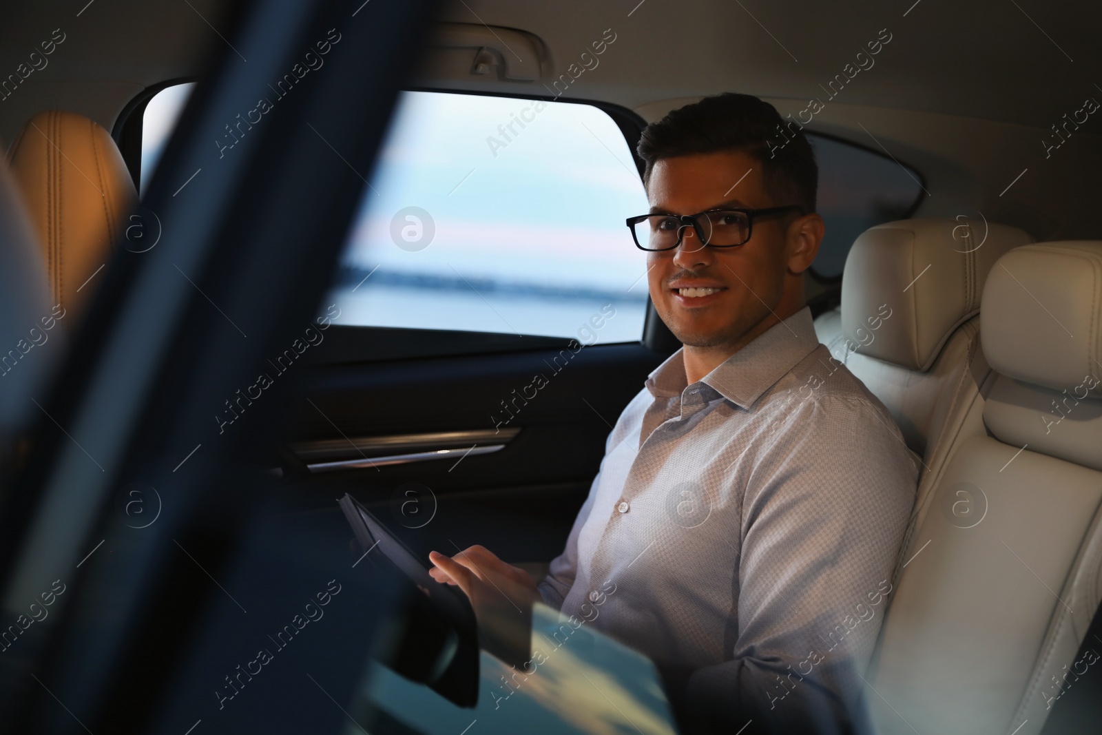 Photo of Handsome man using tablet on backseat of modern car