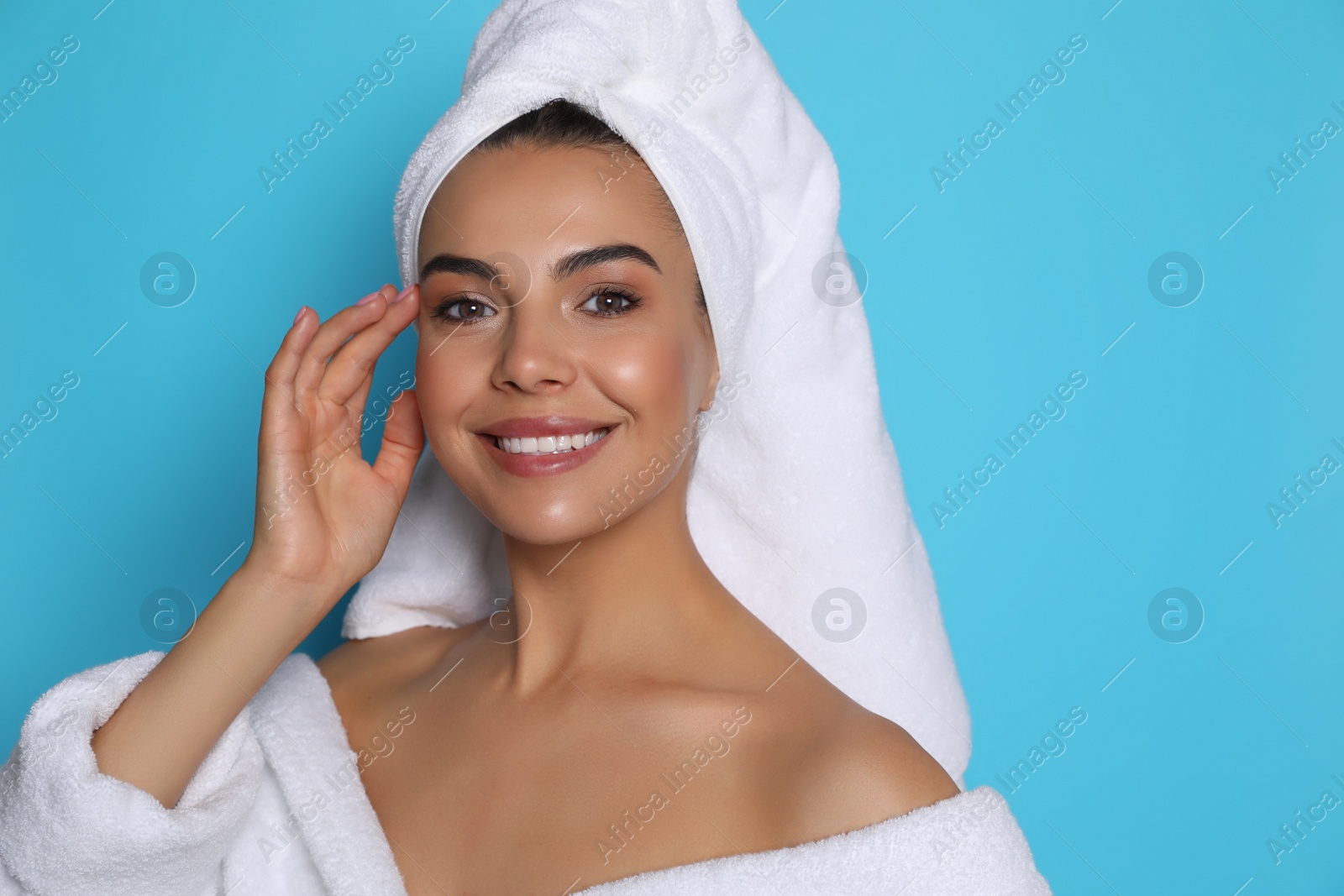 Photo of Beautiful young woman wearing bathrobe and towel on head against light blue background