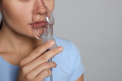 Photo of Sick young woman using nebulizer on grey background, closeup. Space for text