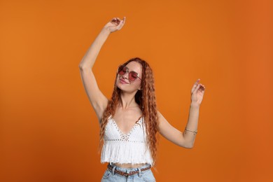 Photo of Stylish young hippie woman in sunglasses dancing on orange background