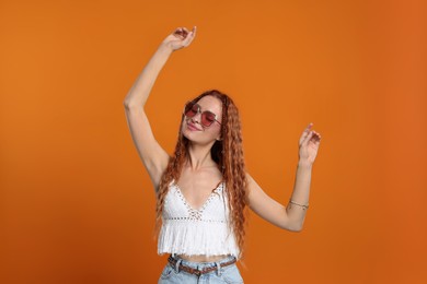 Stylish young hippie woman in sunglasses dancing on orange background