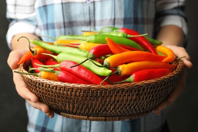 Young woman holding wicker bowl with different hot chili peppers, closeup