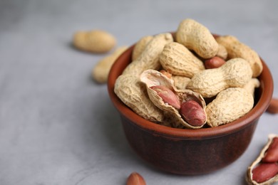 Photo of Fresh unpeeled peanuts in bowl on grey table, closeup. Space for text