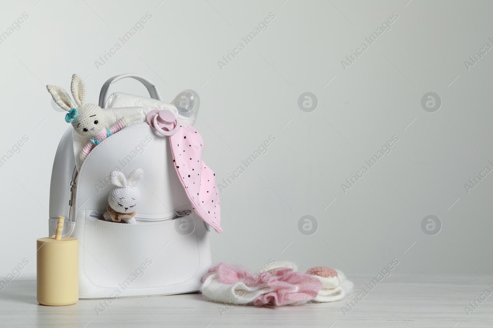 Photo of Mother's backpack with baby's stuff on white wooden table against grey background. Space for text