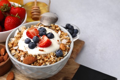 Photo of Tasty granola, yogurt and fresh berries in bowl on light table, closeup with space for text. Healthy breakfast