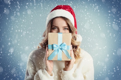 Image of Beautiful young woman in Santa hat with Christmas present on color background