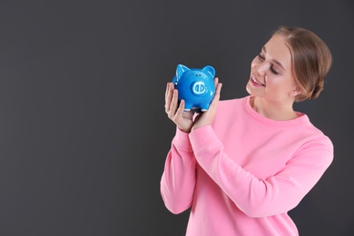 Happy young woman with piggy bank and space for text on grey background. Money saving