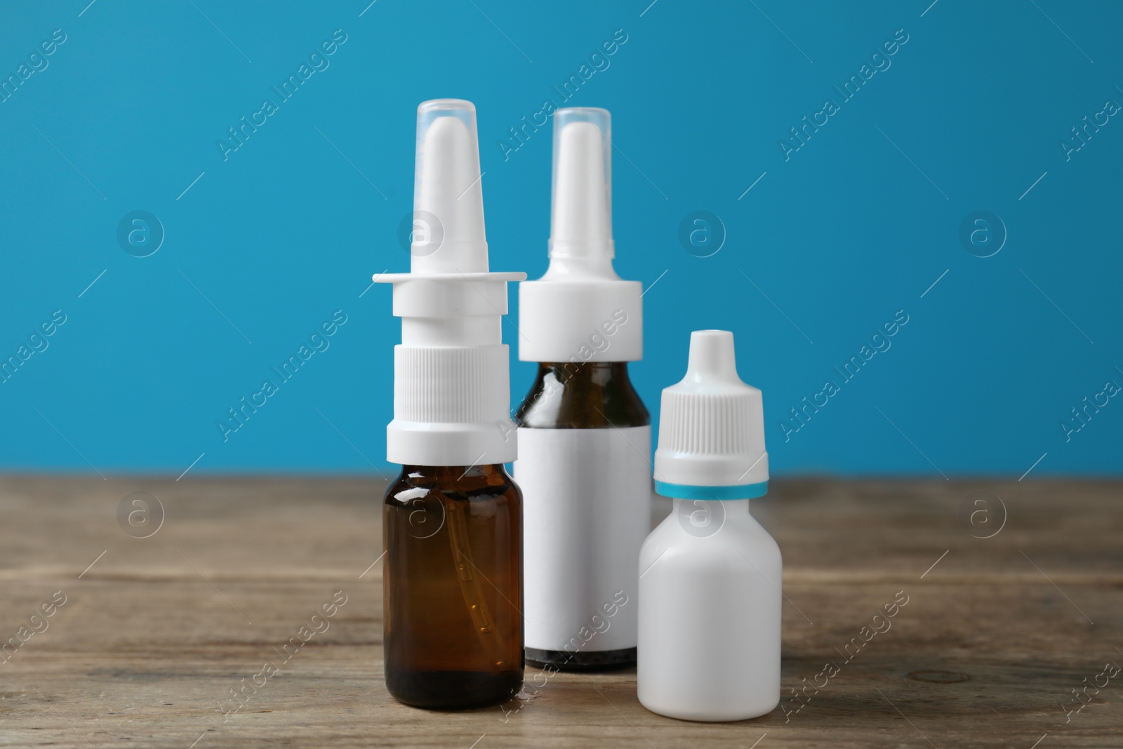 Photo of Nasal sprays in different bottles on wooden table against light blue background