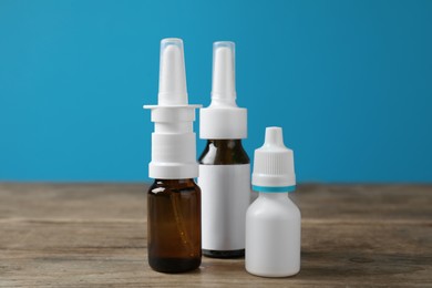 Photo of Nasal sprays in different bottles on wooden table against light blue background