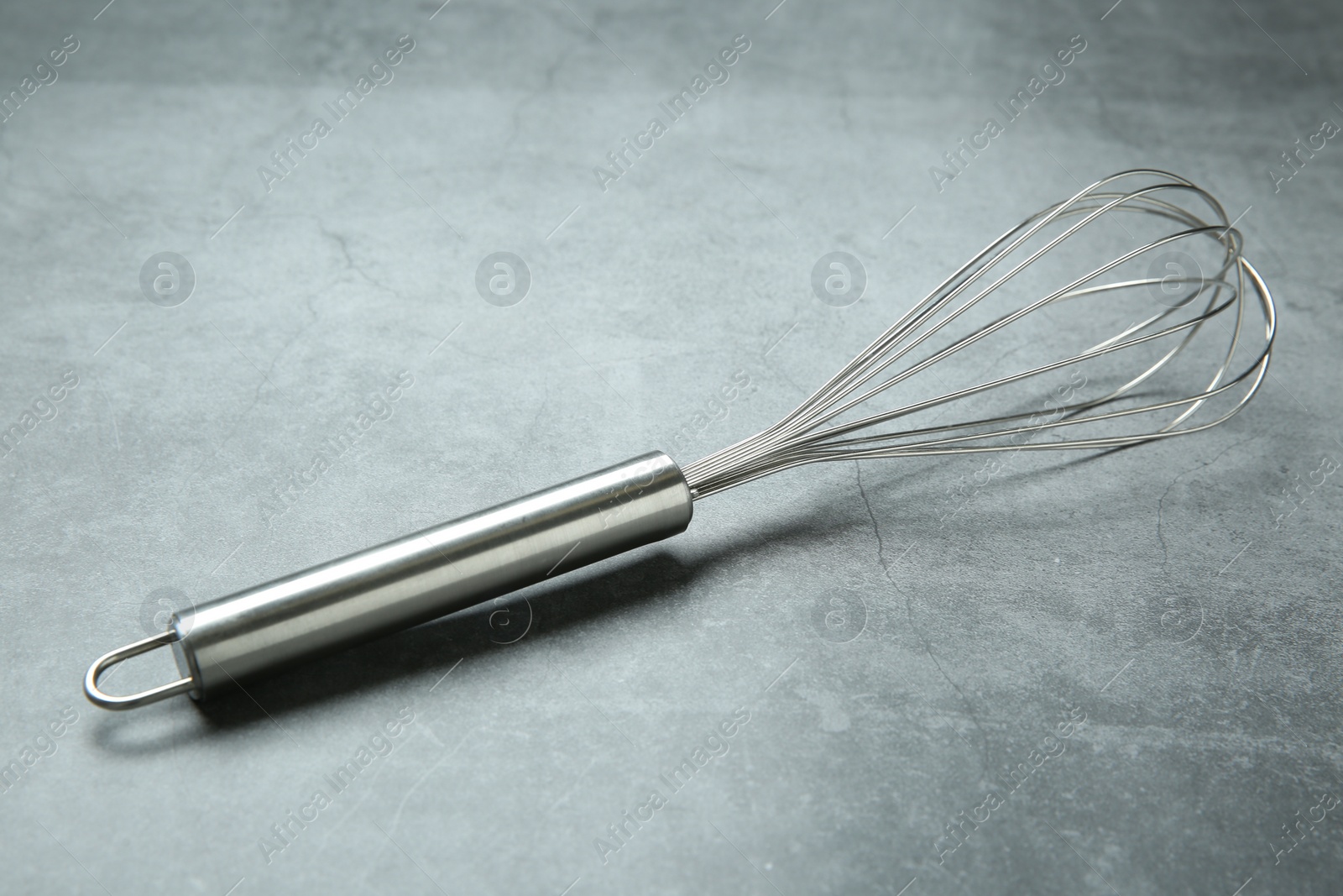 Photo of Metal whisk on gray table. Kitchen tool