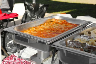 Delicious stuffed cabbage, dumplings and patties in warmers on table outdoors. Volunteer food distribution