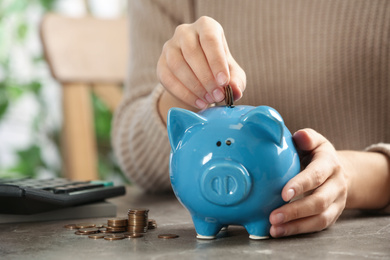 Woman putting money into piggy bank at table, closeup