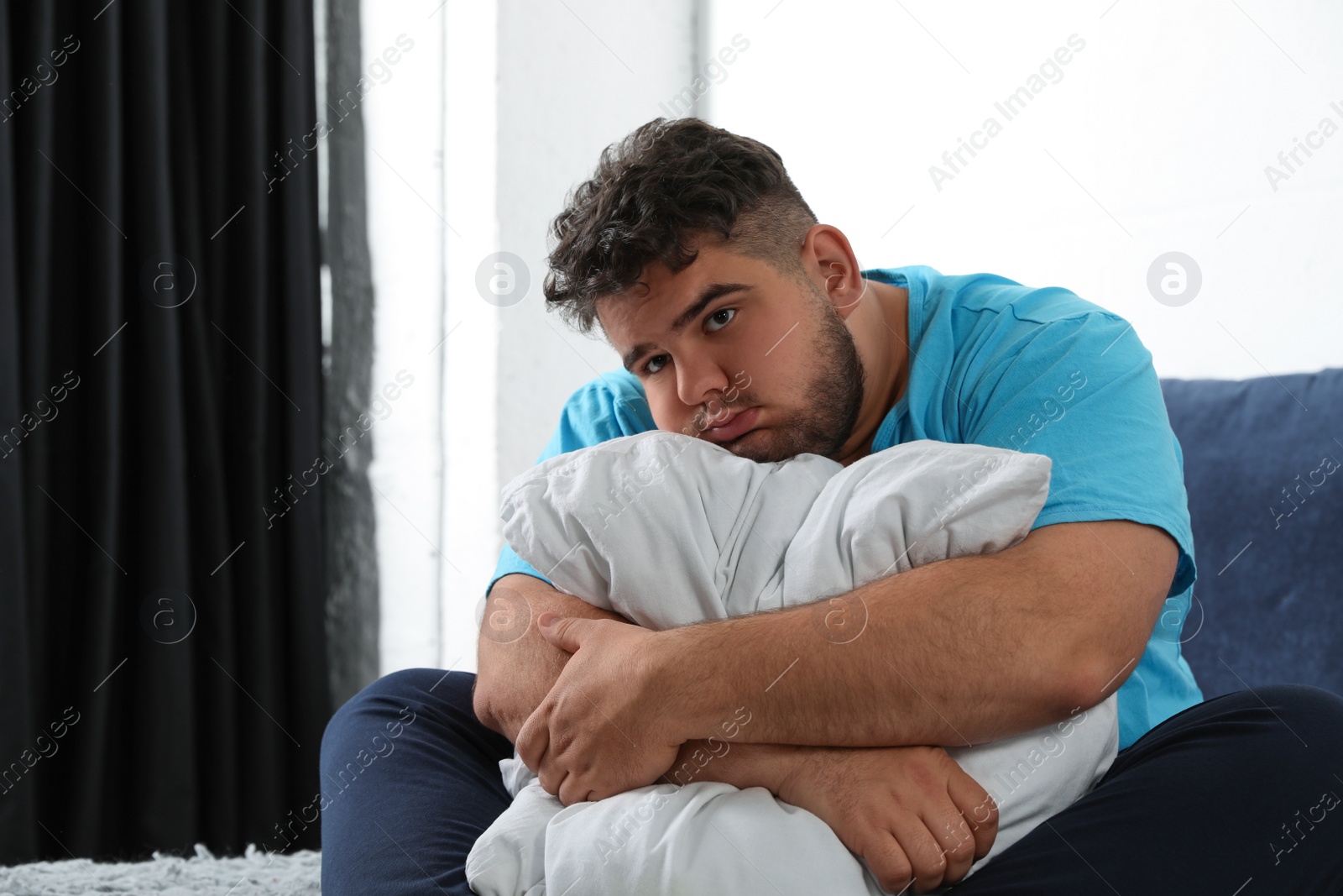 Photo of Depressed overweight man hugging pillow on bed