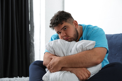 Photo of Depressed overweight man hugging pillow on bed