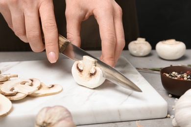 Photo of Young woman cutting fresh champignon mushrooms on marble board, closeup view