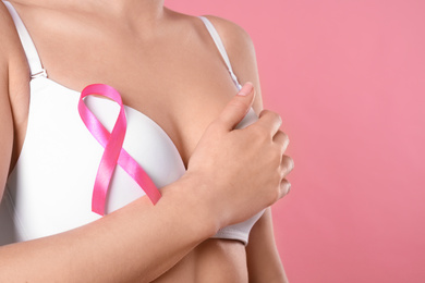 Woman with pink ribbon on color background, closeup. Breast cancer awareness