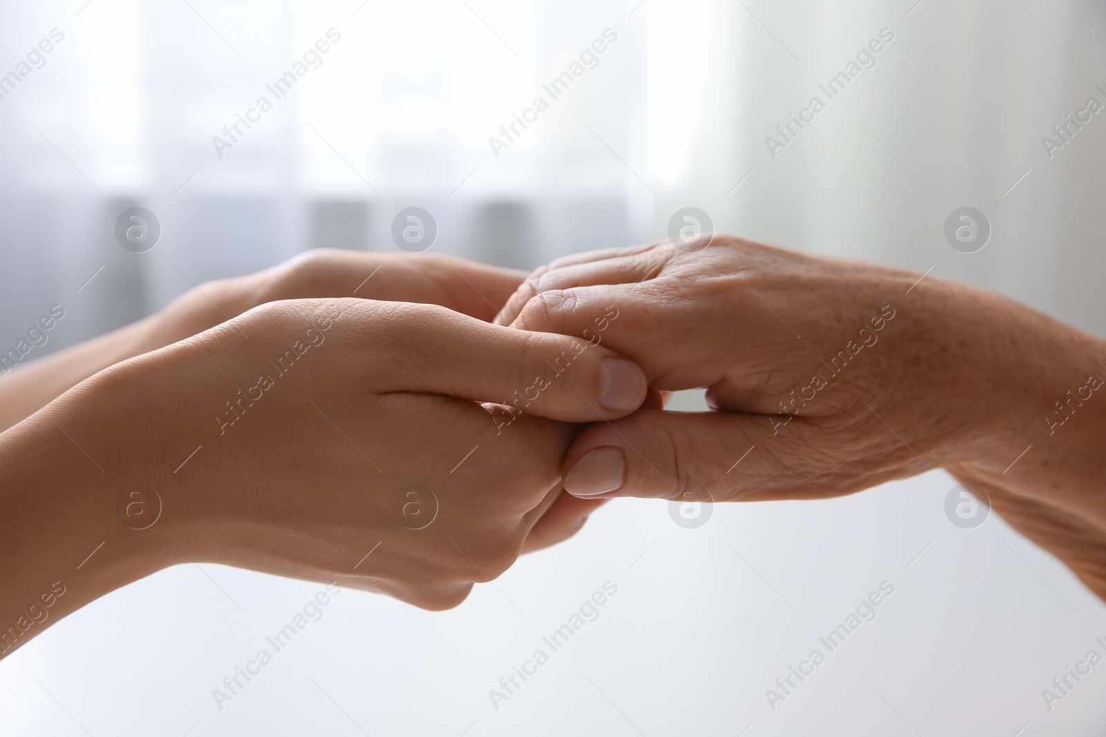 Photo of Young and elderly women holding hands together at home, closeup