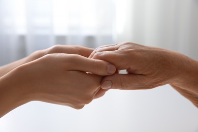 Photo of Young and elderly women holding hands together at home, closeup