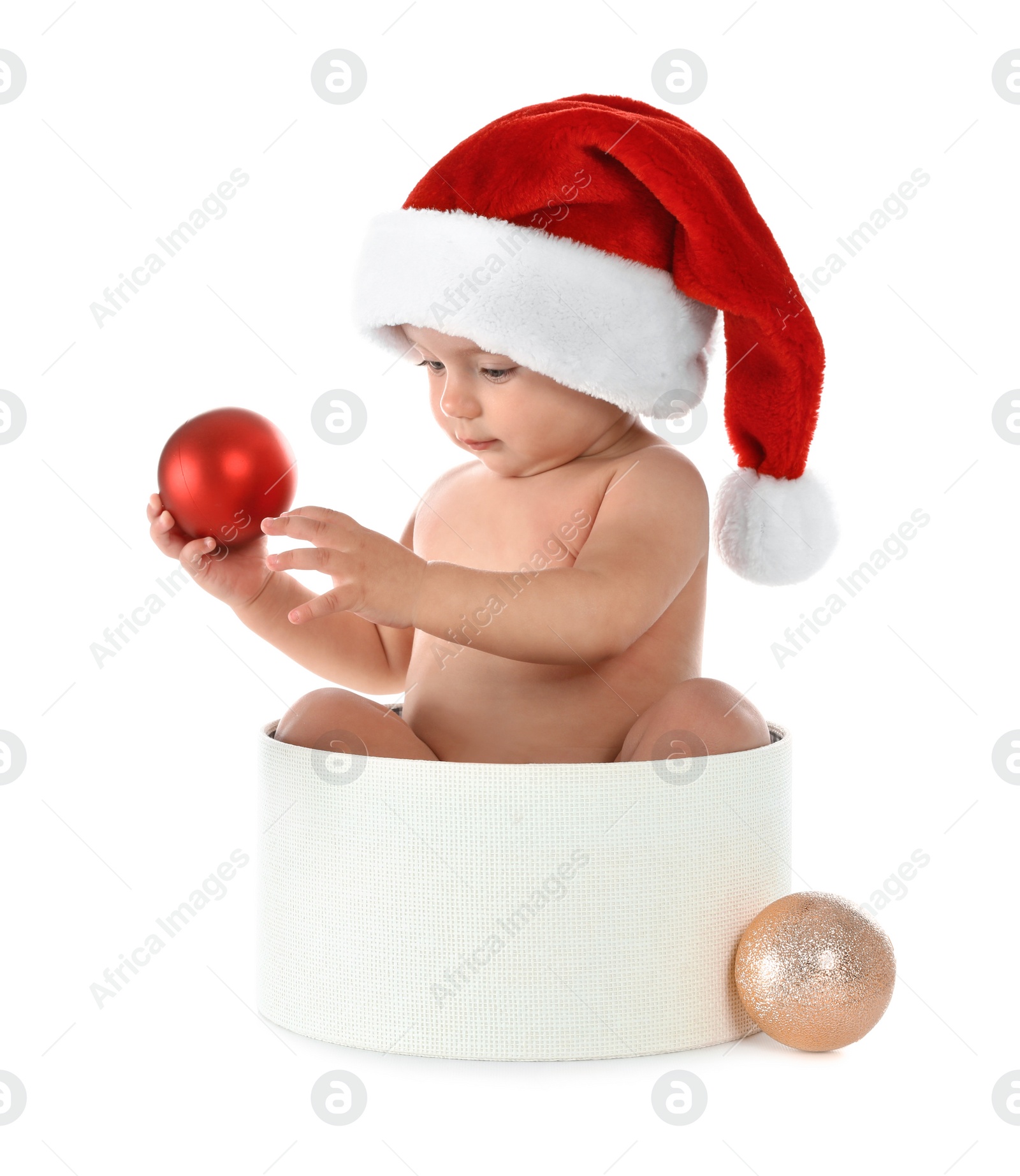 Photo of Cute little baby wearing Santa hat sitting in box with Christmas decorations on white background